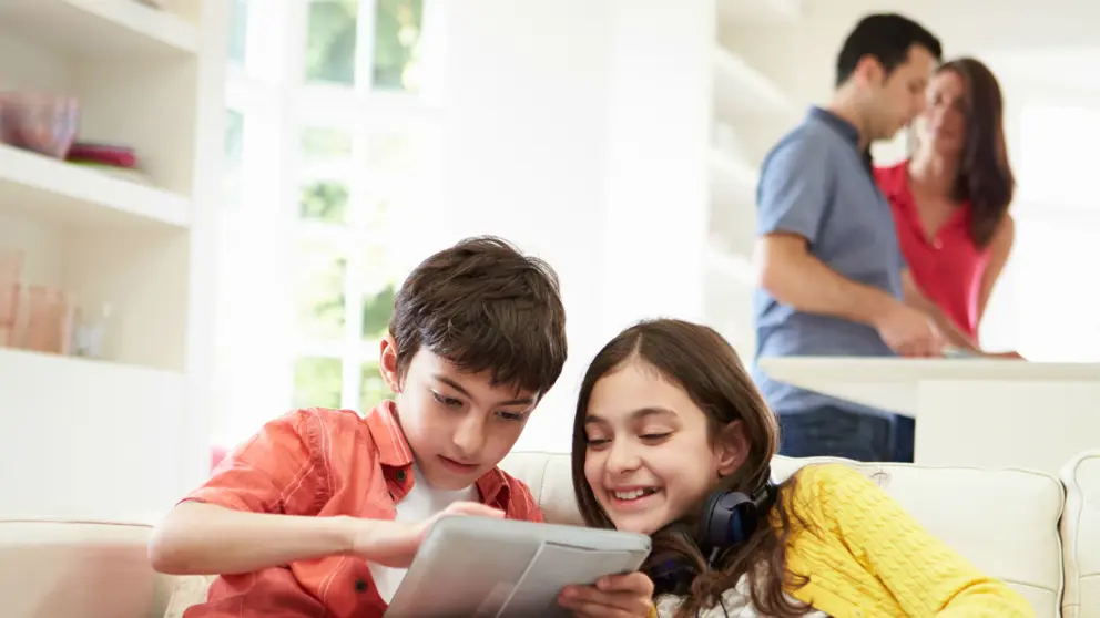 brother and sister playing on tablet while parents prepare dinner