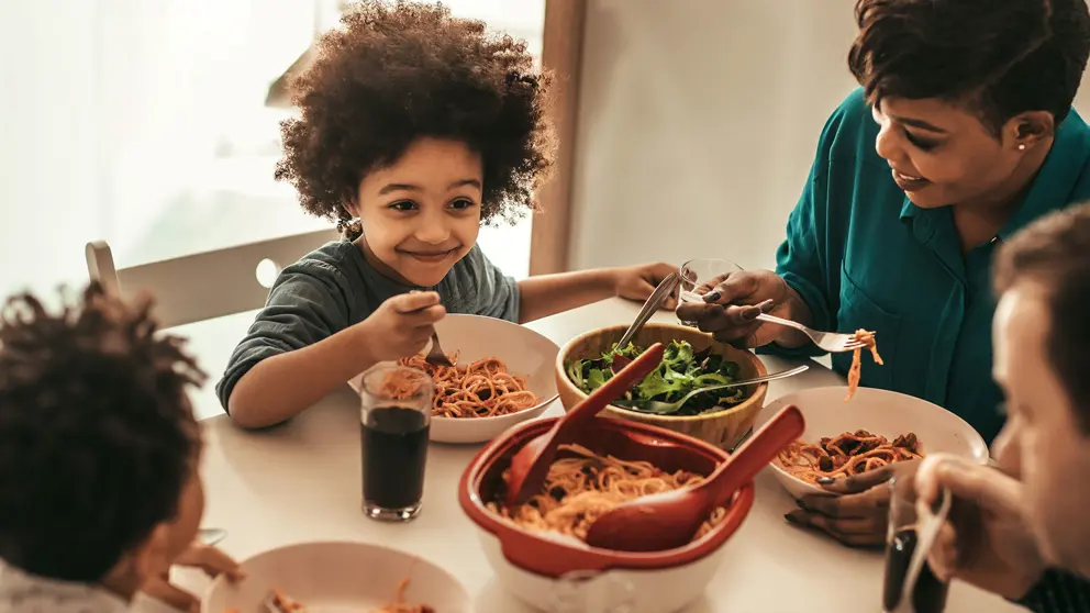  Child smiling at their family around the dinner table eating spaghetti