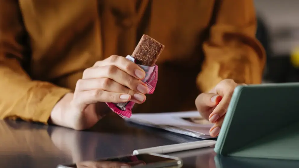 A woman holding a protein bar at a table.