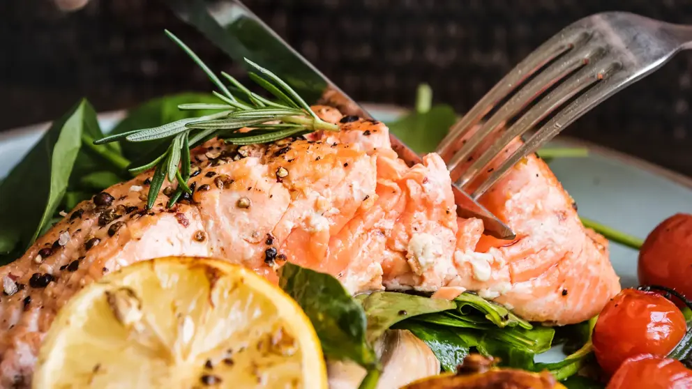 A plate of salmon with a knife and fork cutting into it