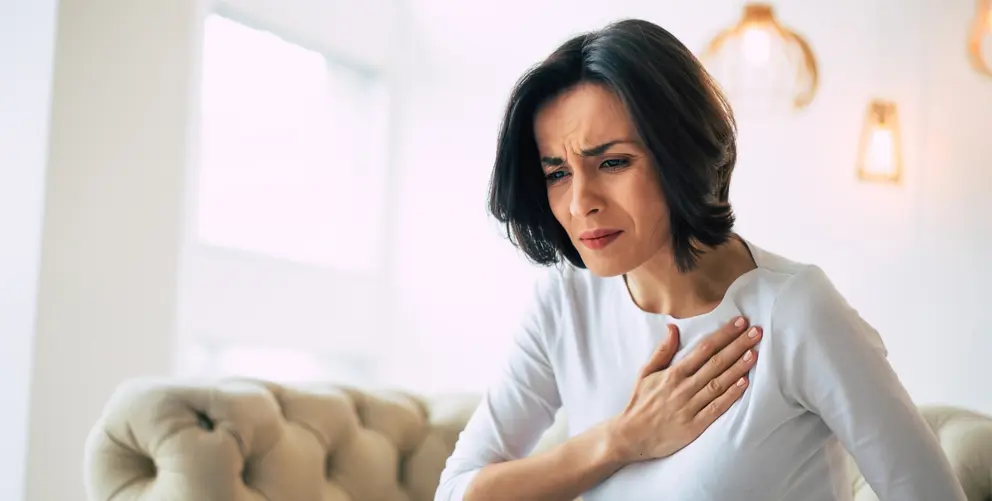 A woman holds her hand to her chest while experiencing discomfort