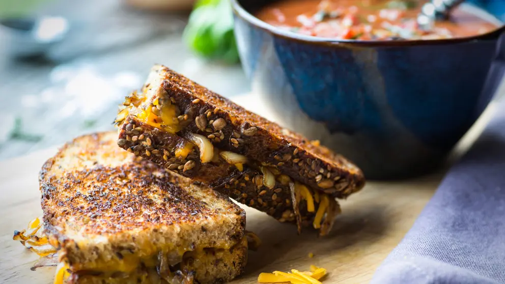 Fresh tomato soup with grilled onion and cheese sandwich on a wooden cutting board.  