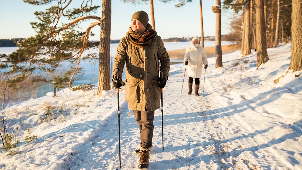 A senior couple walking on a snow covered trail by a lake.