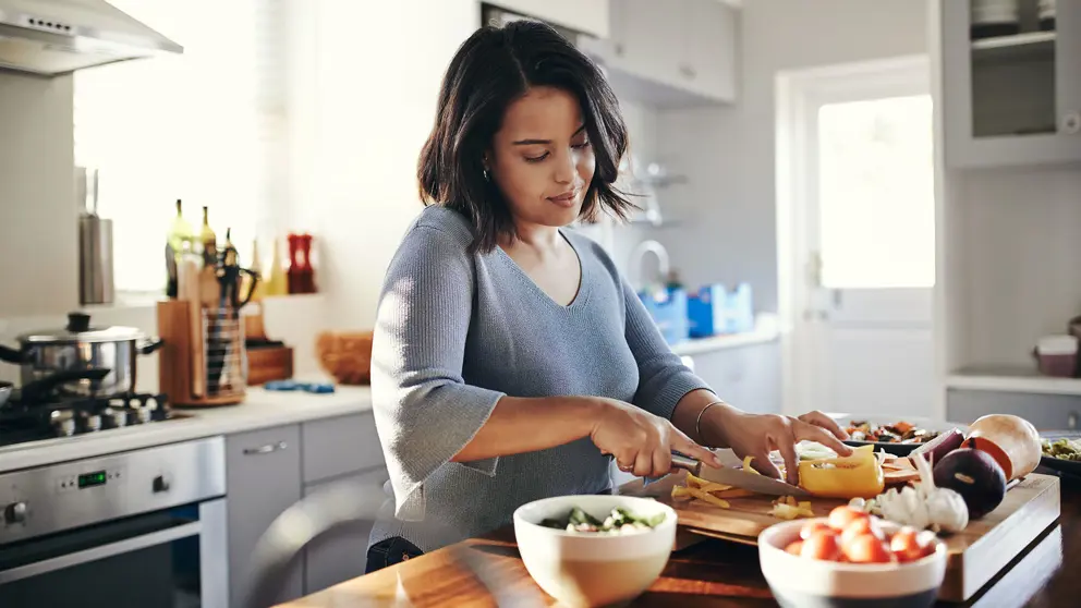 A woman cuts vegetables at her kitchen counter