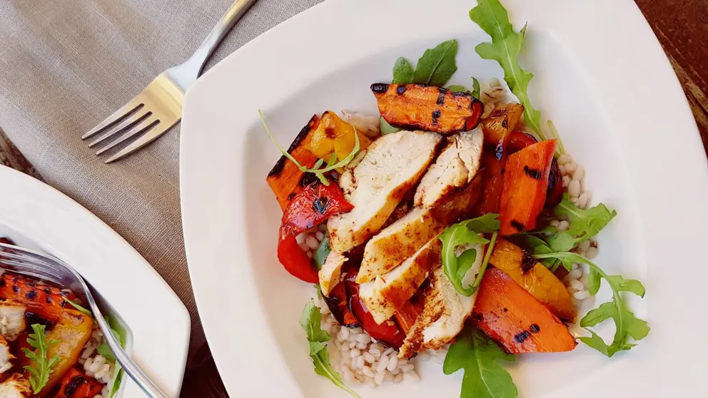 Grilled chicken barley bowl on a white plate with a silver fork