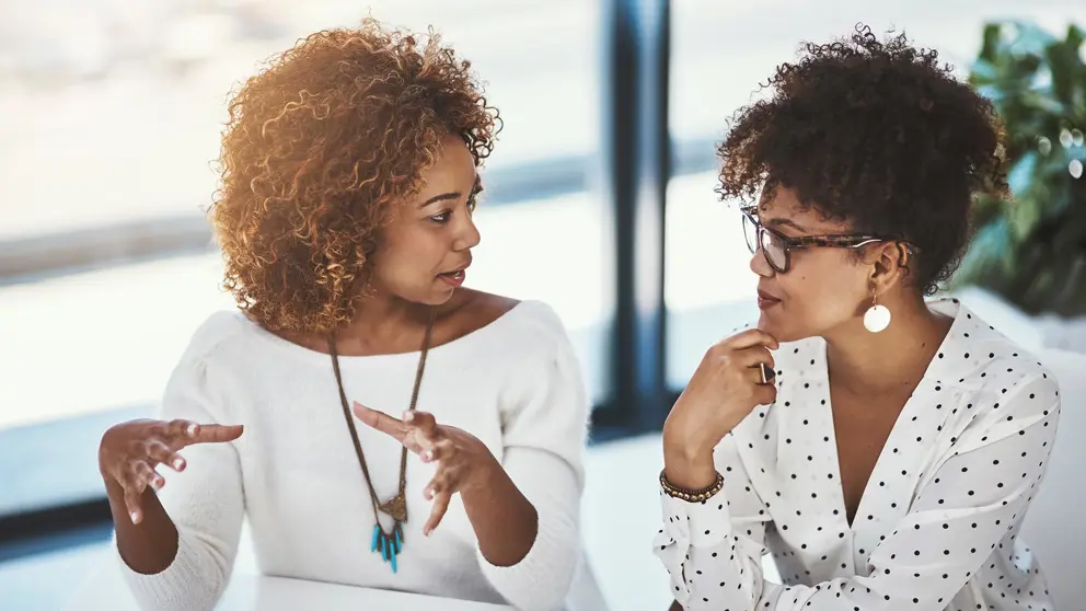 Two professional women talking to one another sitting in a boardroom