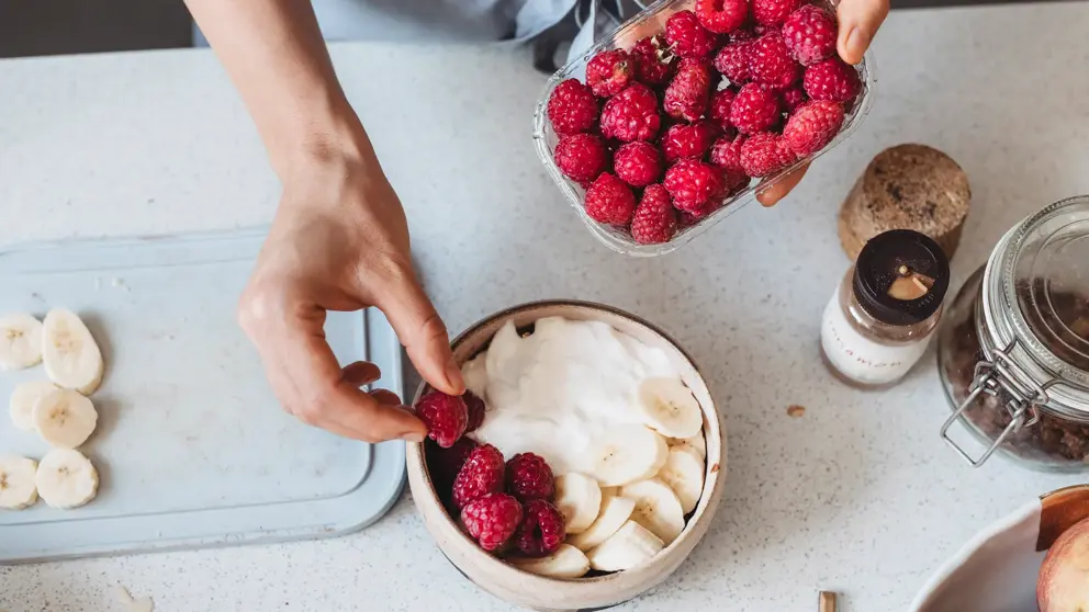 A person placing strawberries in a bowl with yogurt and bananas.