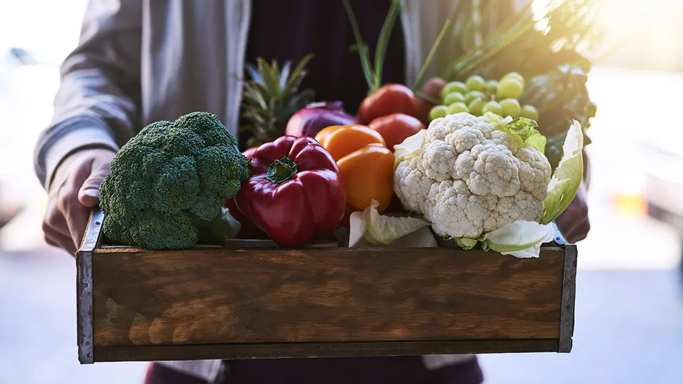 Woman holding wooden box with vegetables