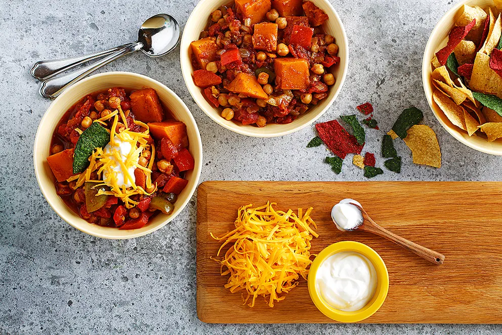 Bean, sweet potato and garlic stew in a red serving dish with bowls alongside