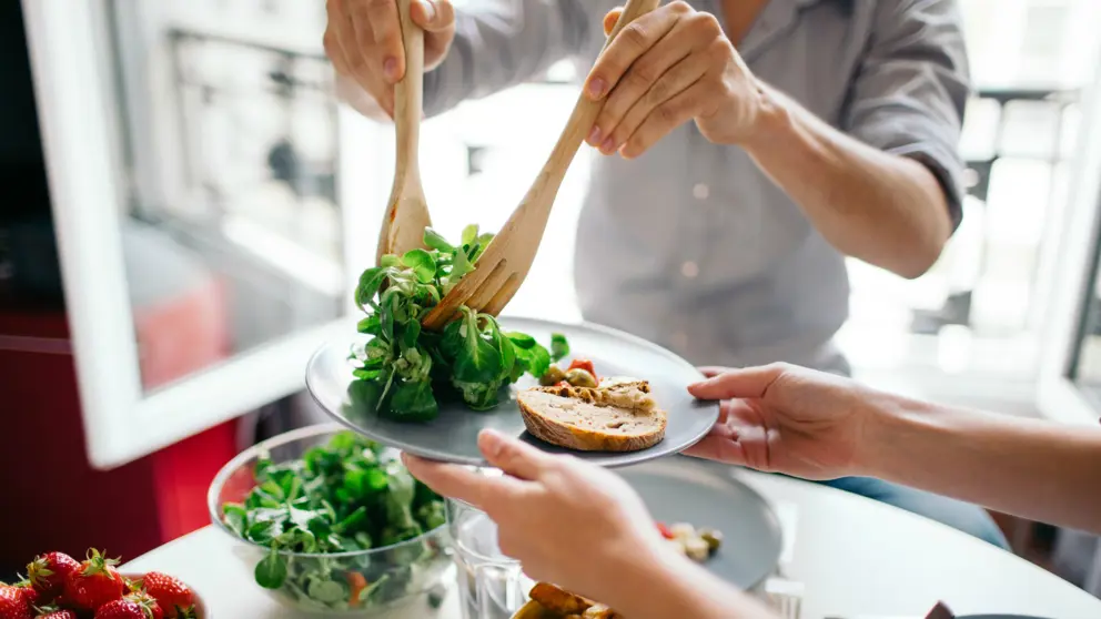 A man puts salad on a white plate with bread.