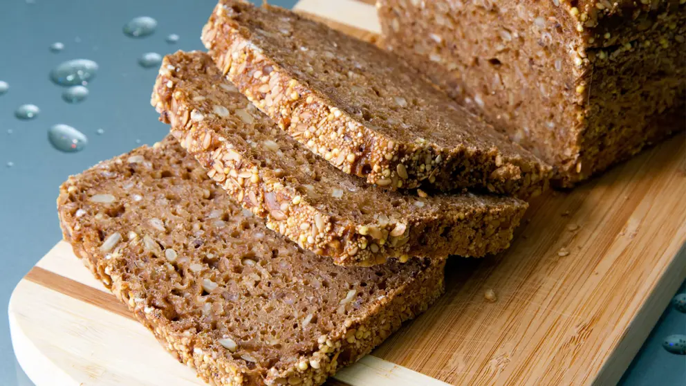 Loaf of whole grain bread and slices on wooden cutting board