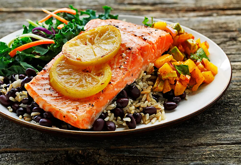 Plate of roasted trout, mango salsa, rice, black beans and green salad