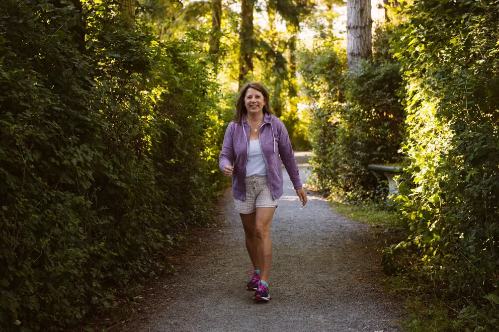 Tracy Bawtinheimer wears a purple jacket and shorts as she walks in the woods.