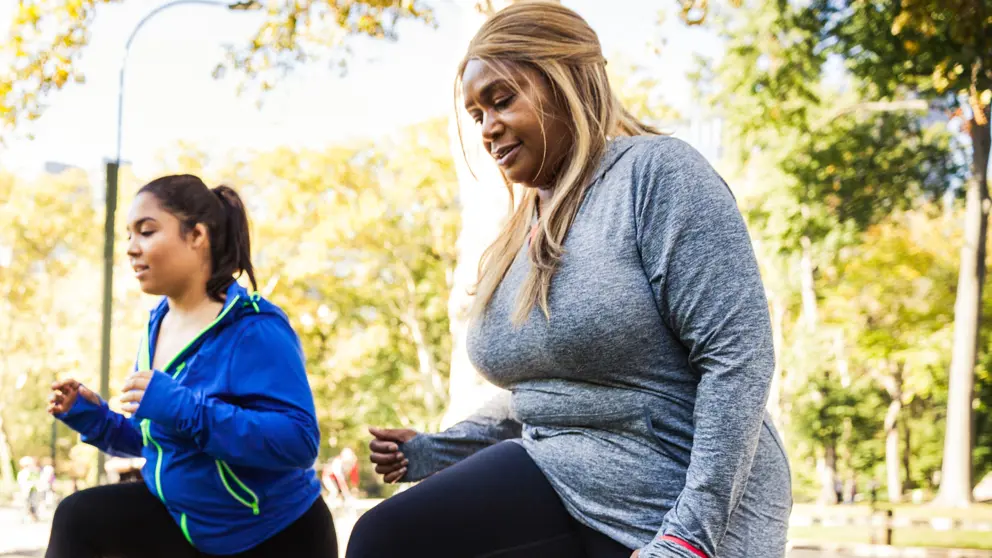 Two women doing lunges on park bench outdoors