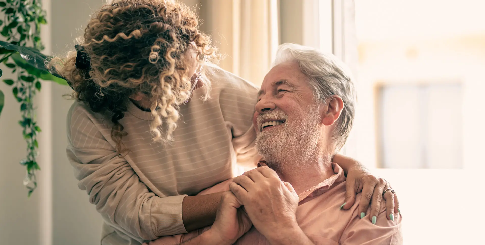 A mature daughter holding her father’s hands while he smiles at her.