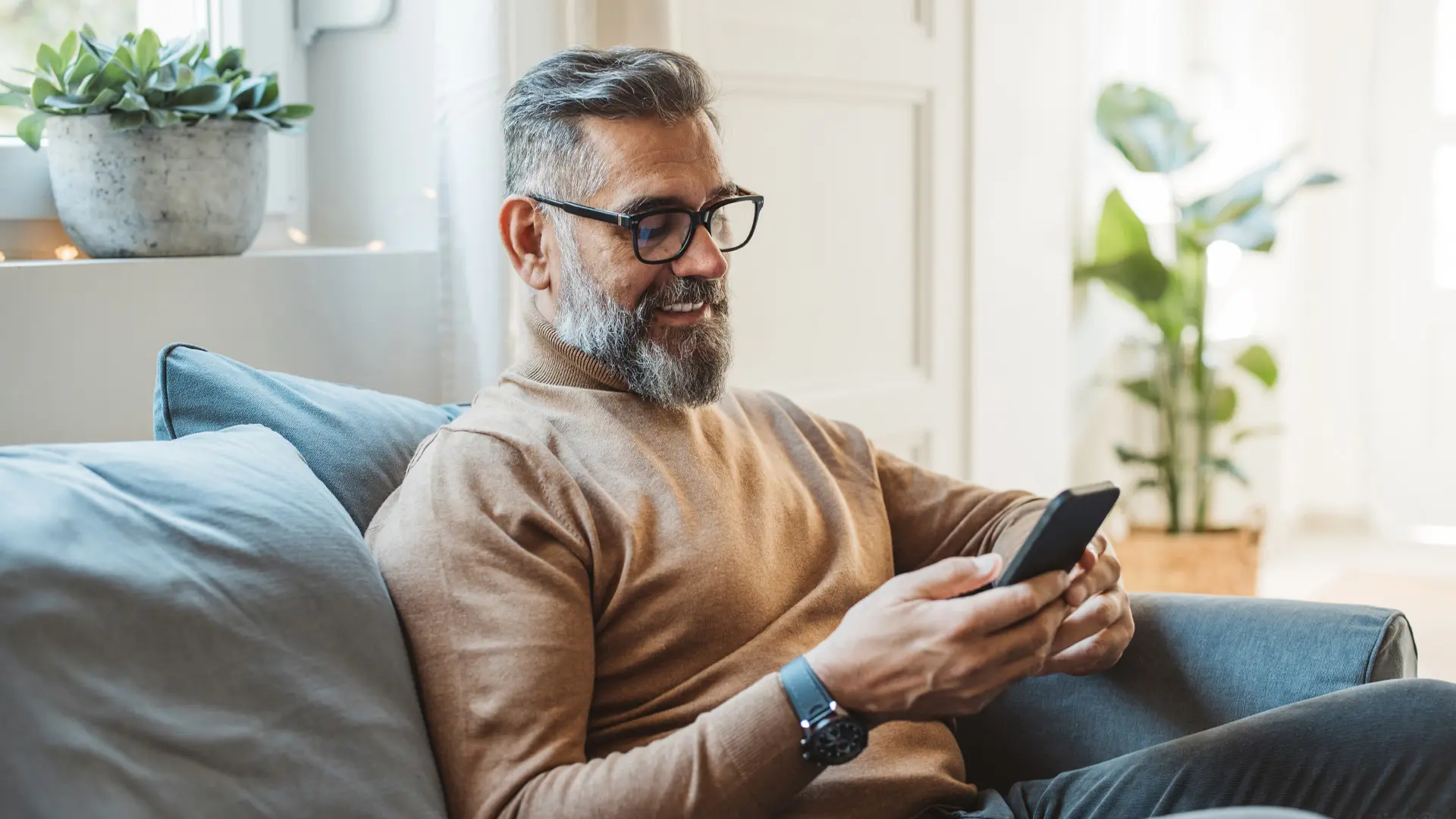 A man using his phone while seated on a couch.