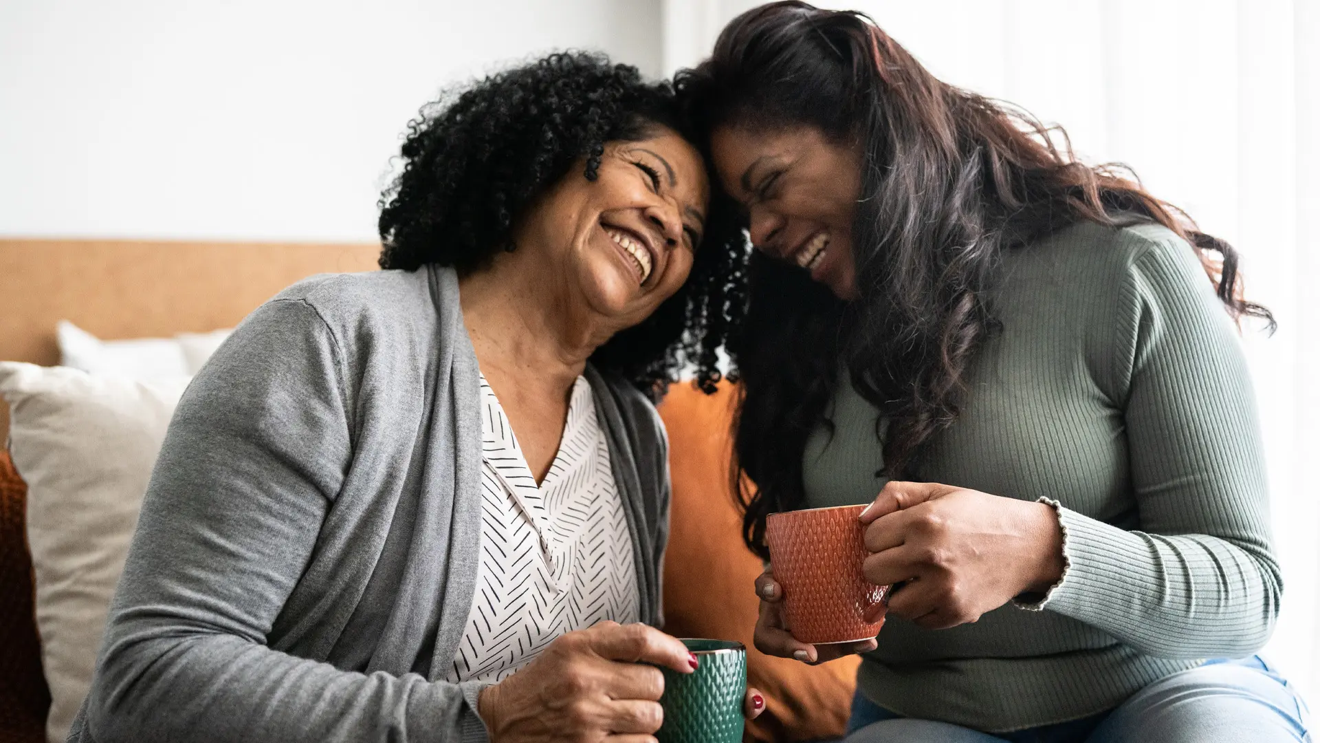 Two women having an intimate laugh while holding mugs.