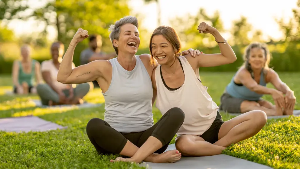 Two women laugh while holding each other and flexing their arms.