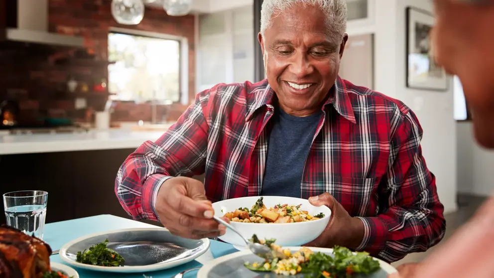 A senior man serving food from a bowl at a table.