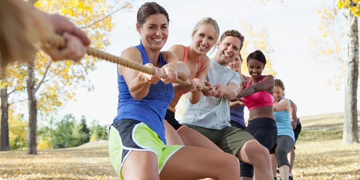 A team of smiling people tugging a rope while outdoors.
