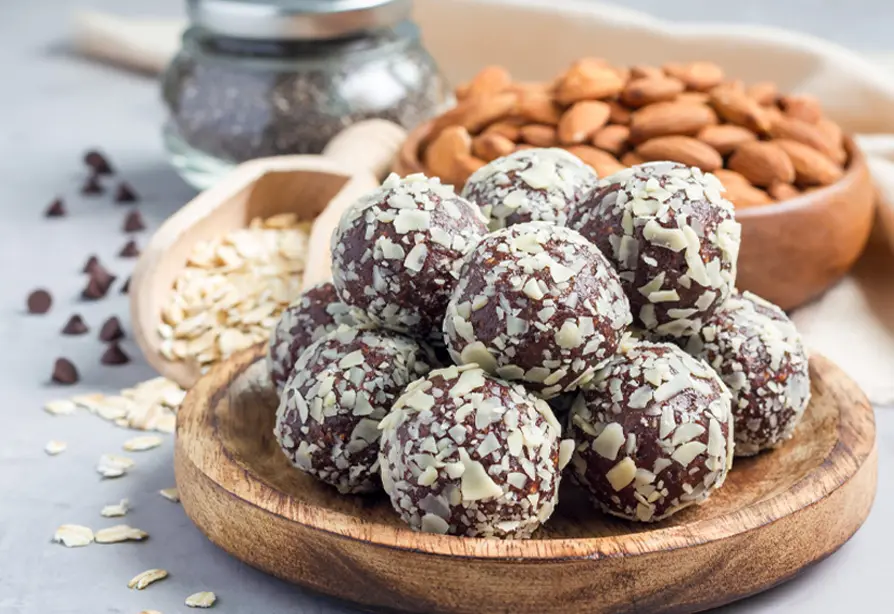 A dish with chocolate almond bites with almonds, chocolate chips and oats on the side.