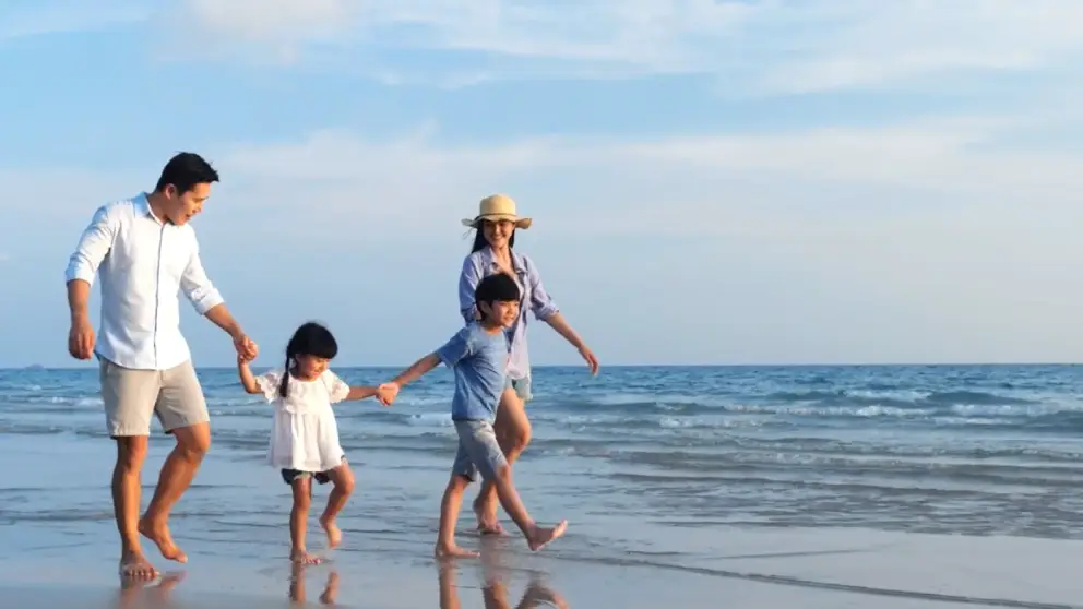 Asian family of 4 walking on the beach, holding hands