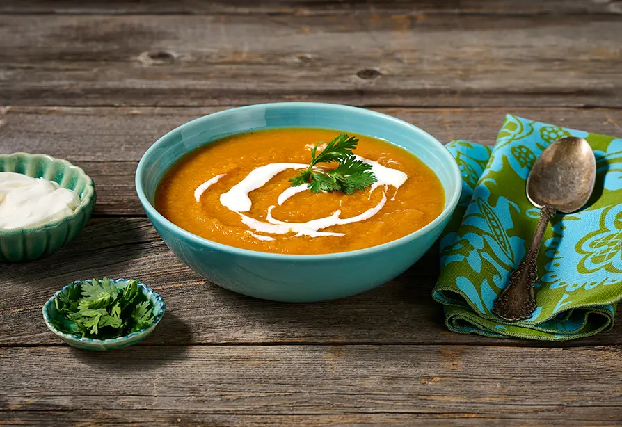 Carrot squash soup in a bowl with garnish of yogurt and cilantro.